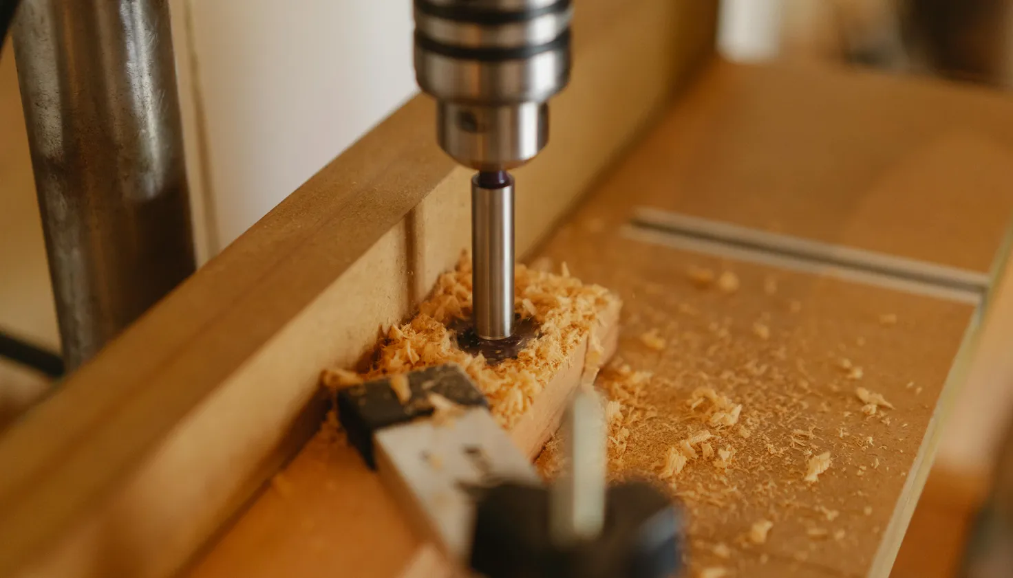 A closeup of a drill drilling into a piece of wood with sawdust around it
